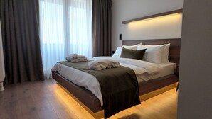 A modern hotel room with a wooden bed, a bedside table, a nightstand, and a large window with curtains. - Yıldız Termal Otel (Bursa)
