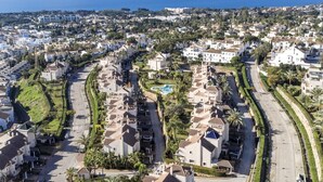 Ein Küstenwohngebiet mit weißen Gebäuden, einer gewundenen Straße und freiem Blick auf das Meer.