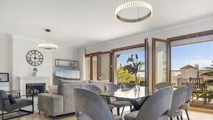 Ein modernes Wohnzimmer mit Kamin, grauen Sofas, einem Glastisch mit Stühlen und großen Fenstern mit Blick ins Freie.