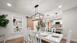 A dining area with a white table, chairs, and a hanging light fixture.