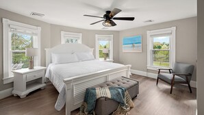 A bedroom with a large bed, a ceiling fan, a chair, and a window with a view.