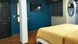 Een slaapkamer met een bed, een aan de muur bevestigde televisie, een raam met zonwering en een spiegel.