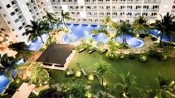 Un hotel moderno de gran altura con varios balcones, piscina y abundante vegetación.