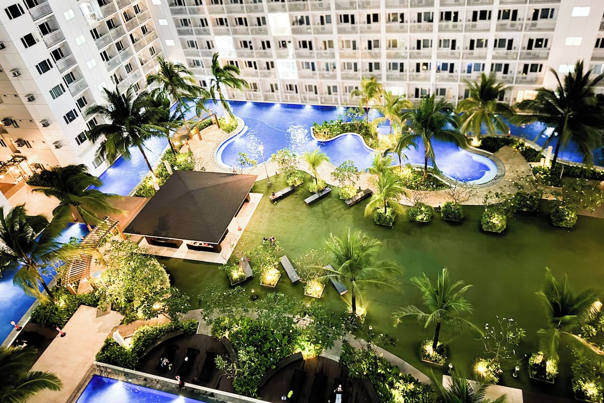 A high-rise hotel with multiple balconies, a swimming pool, and lush landscaping.
