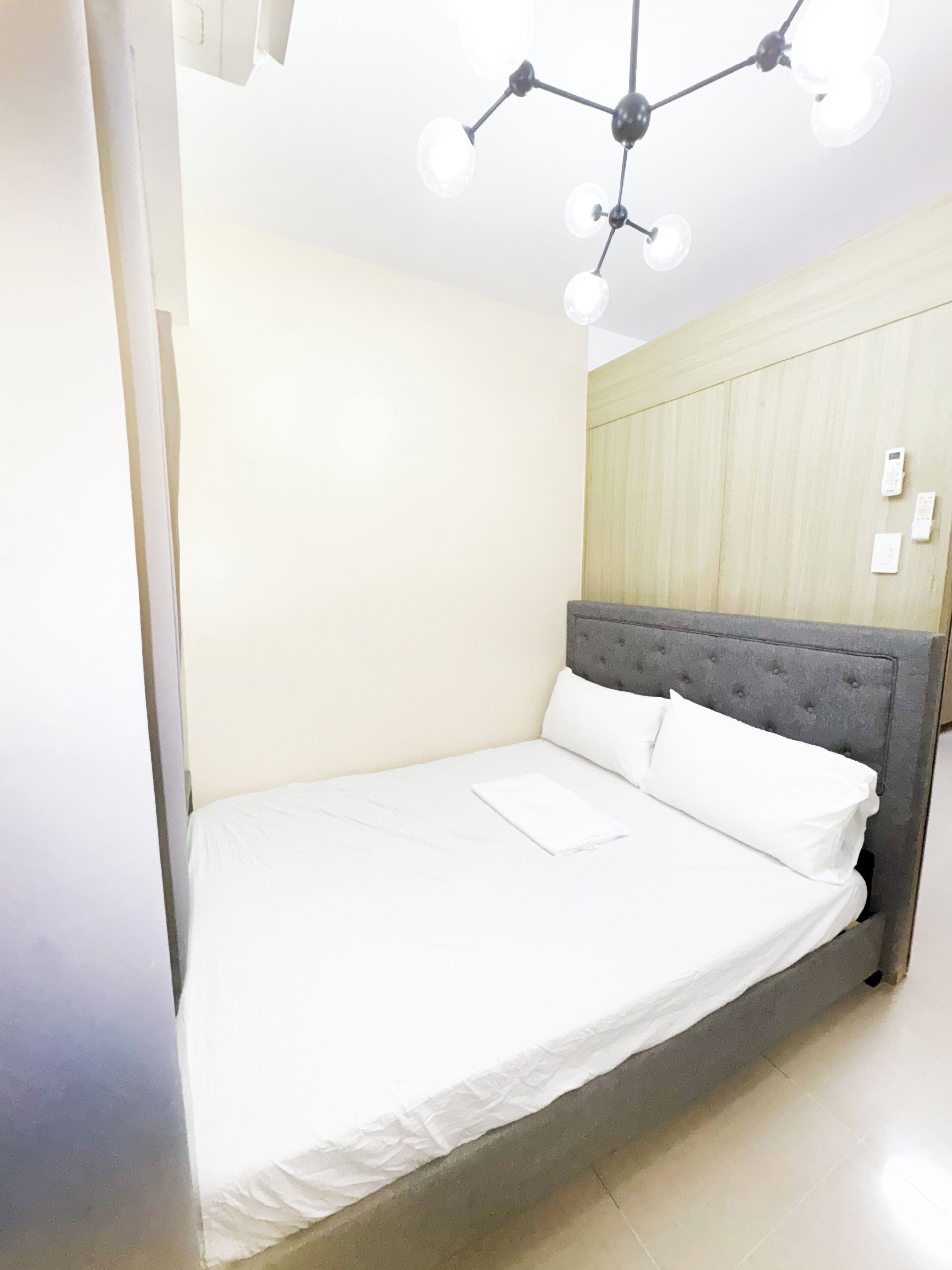 Cama bem arrumada com lençóis brancos num quarto com paredes claras e um detalhe em painel de madeira.