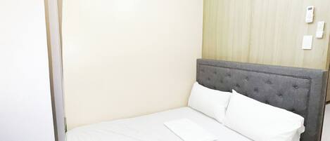 Un lit bien fait, avec du linge de lit blanc, dans une pièce aux murs de couleur claire et agrémentée d’un panneau décoratif en bois.