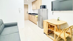 Una cocina moderna con refrigerador, microondas y armarios de madera. Hay una mesa de comedor con sillas y un sofá gris en la zona de estar.