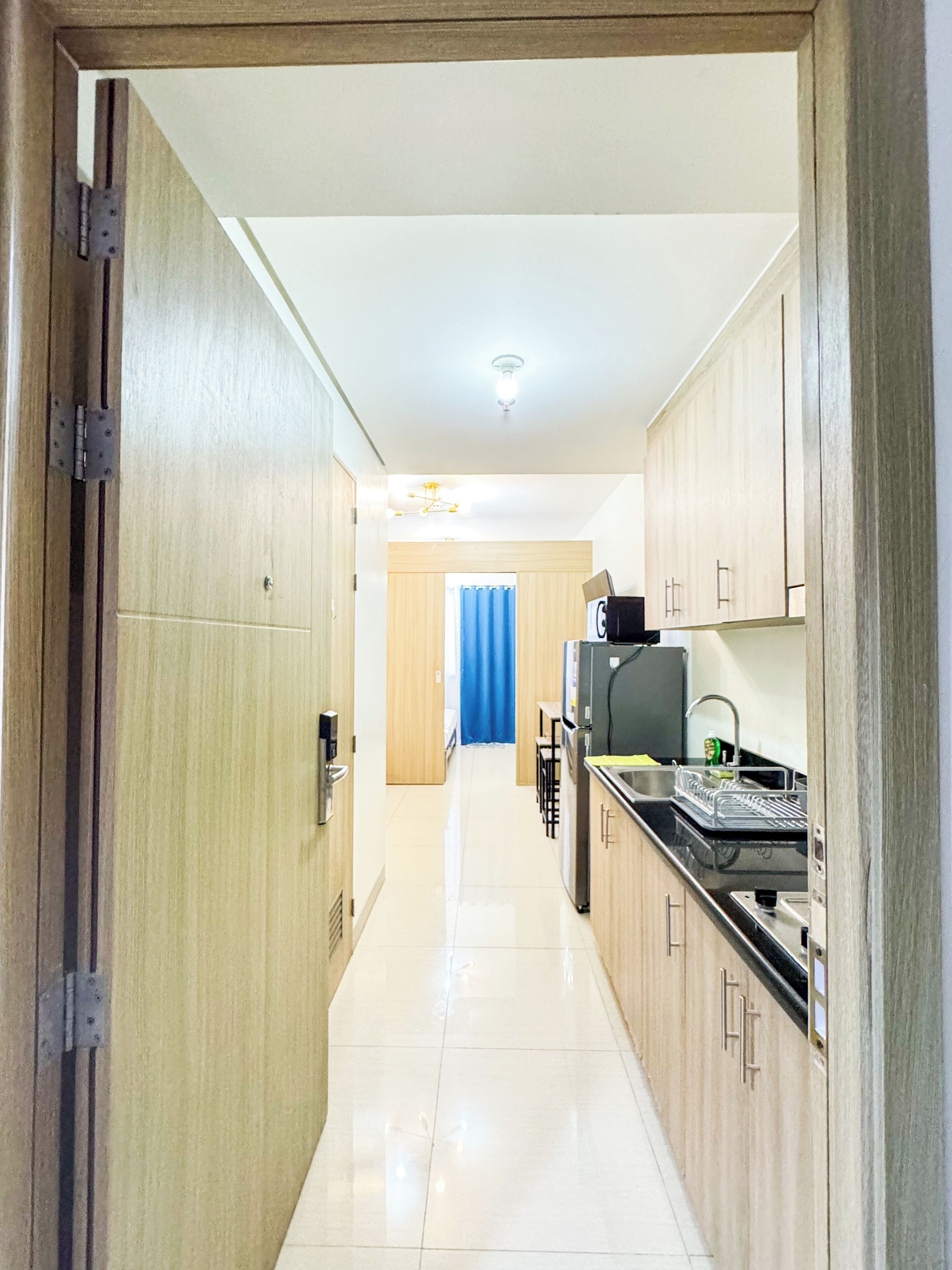 A narrow hallway leading to a kitchen with wooden cabinets, a refrigerator, and a sink.