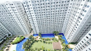 Un edificio de gran altura con múltiples balcones, una piscina central y zonas verdes circundantes.