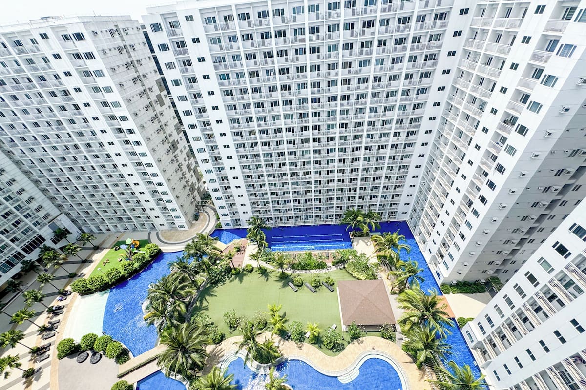 A high-rise building with multiple balconies, a central swimming pool, and surrounding greenery.