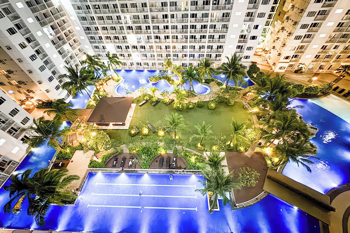 A rooftop pool surrounded by palm trees and a high-rise building.