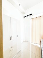 A bright, white room with a wardrobe, a shower curtain, and an air conditioning unit.
