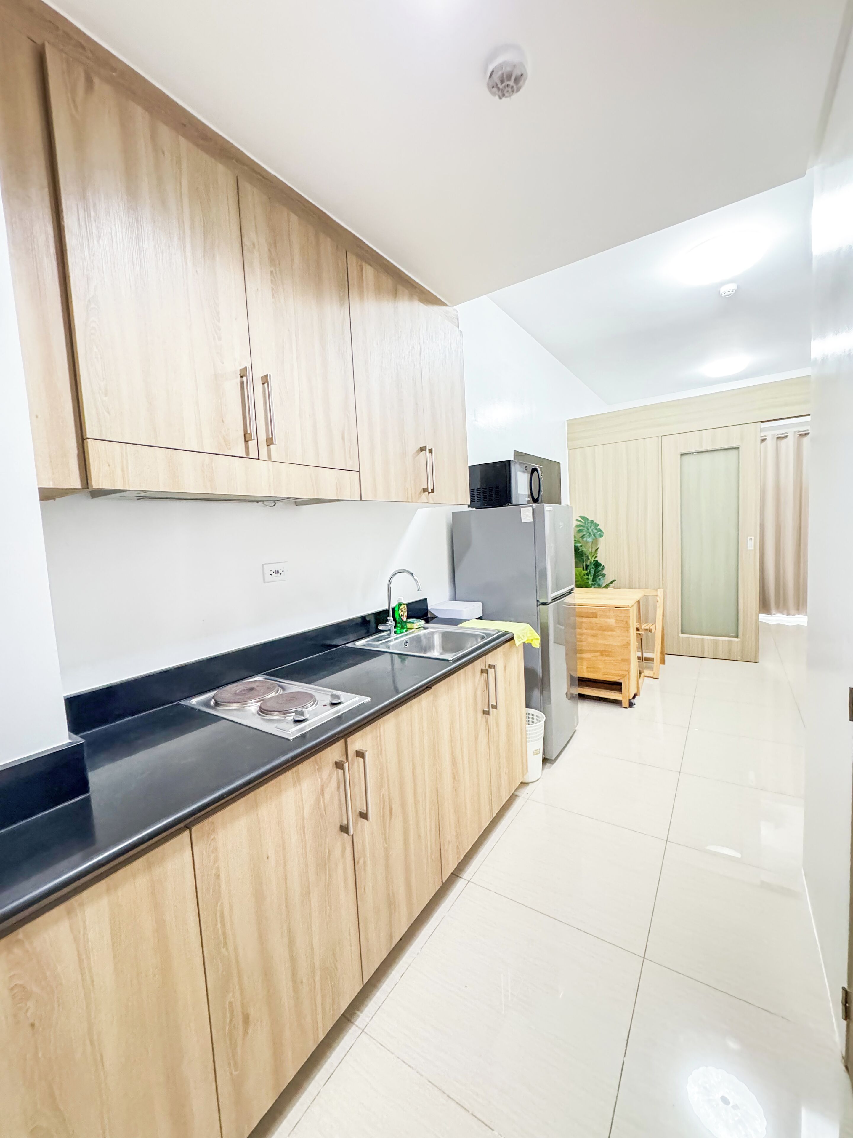 Una cocina moderna con armarios de madera, encimera negra, electrodomésticos de acero inoxidable y suelo de baldosas.