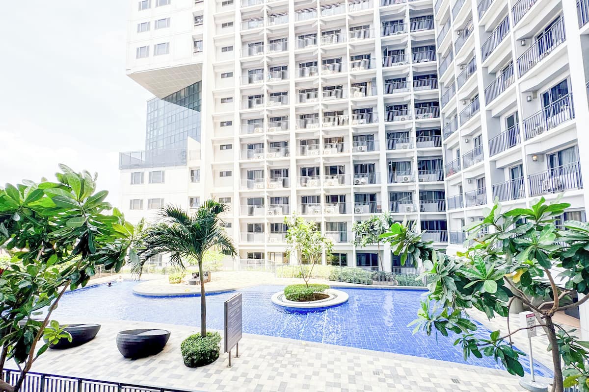 A modern building with a pool area, surrounded by greenery and a fenced walkway.