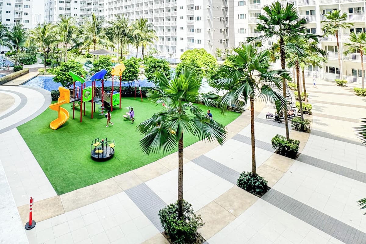 A residential area with high-rise apartment buildings, a playground with slides, and palm trees.
