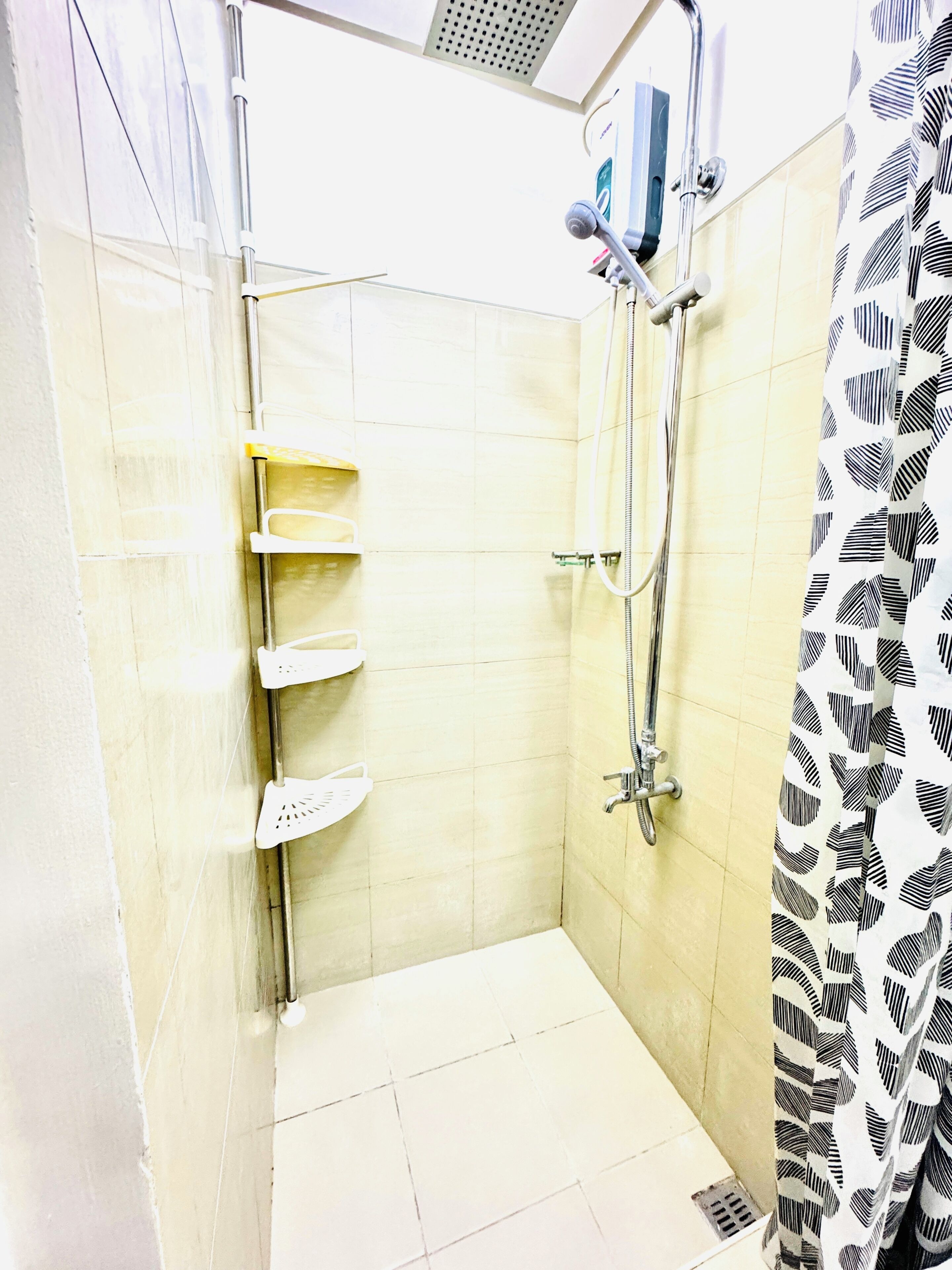 Una ducha con cabezal de ducha manual, grifo empotrado y cortina de baño con estampado de hojas.