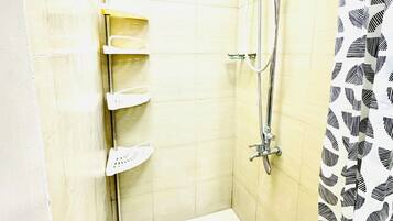 Una ducha con cabezal de ducha manual, grifo empotrado y cortina de baño con estampado de hojas.