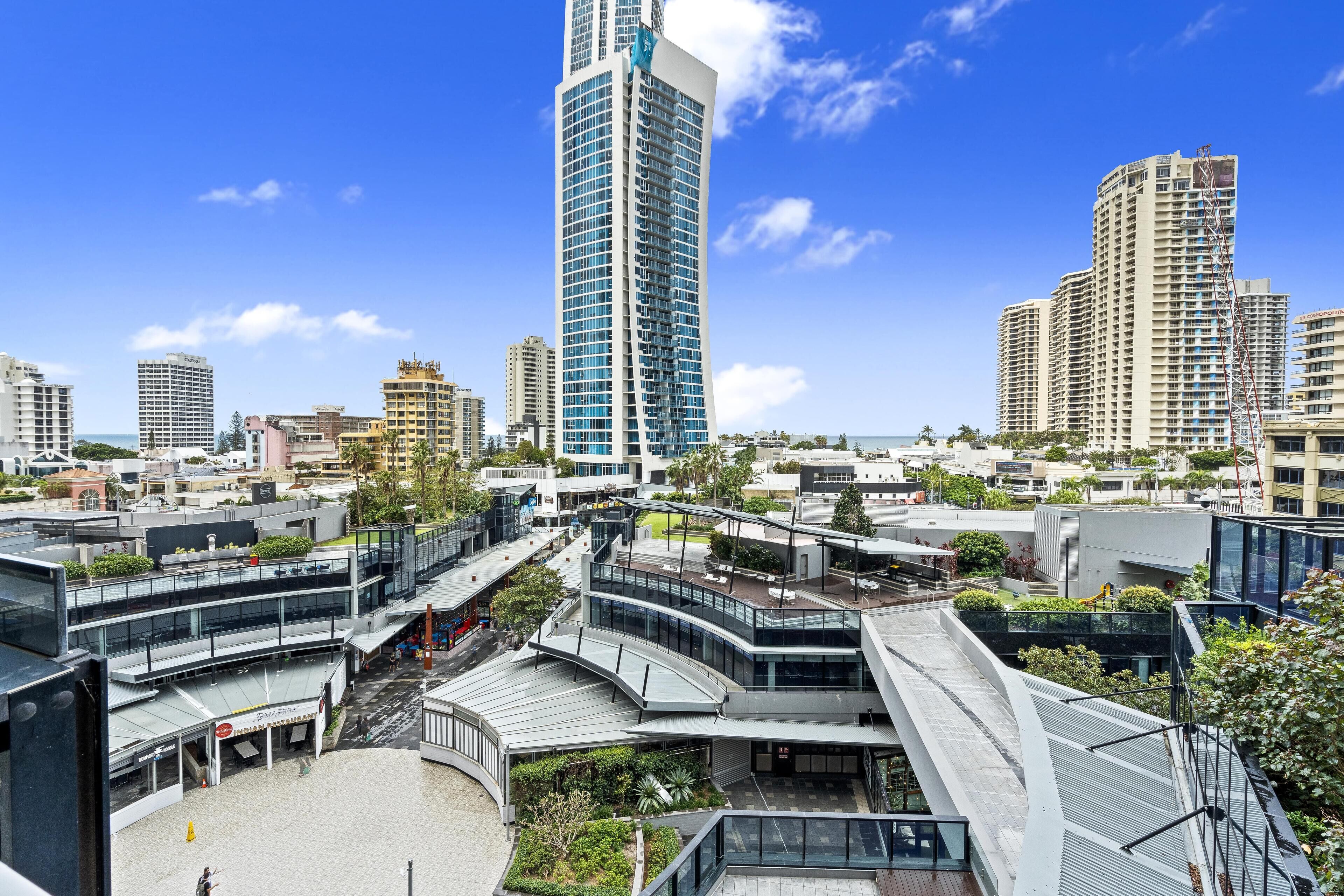 Un quartier urbain moderne, avec de hauts immeubles, un pont piétonnier central et une vue sur le front de mer.