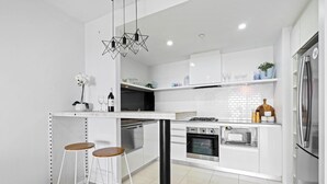 A modern kitchen with white cabinetry, a central island with stools, stainless steel appliances, and a geometric pendant light.