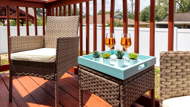 A wicker chair and table on a wooden deck with a railing, two glasses of amber liquid, and small potted plants. - Summer Safari - GORGEOUS Home Near Busch Gardens & USF (Tampa)