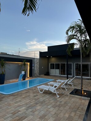 Un área de piscina exterior moderna con una fuente, sillas de descanso y plantas en macetas.