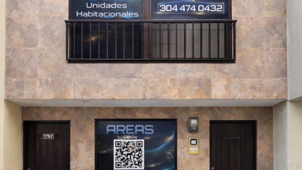 Eine Gebäudefassade mit zwei Schildern, die 'AREAS by QuBe Lab' bewerben, und einem QR-Code.