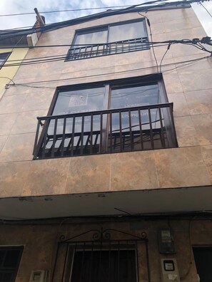 Un edificio con fachada de tejas, un balcón con barandilla de metal y una entrada con portón.