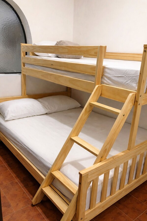 Una cama litera con estructura de madera, ropa de cama blanca y un ventanal pequeño.