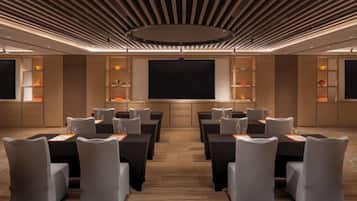 Un salón de conferencias con diseño moderno, que incluye una pantalla grande, varias mesas y sillas dispuestas para presentaciones.