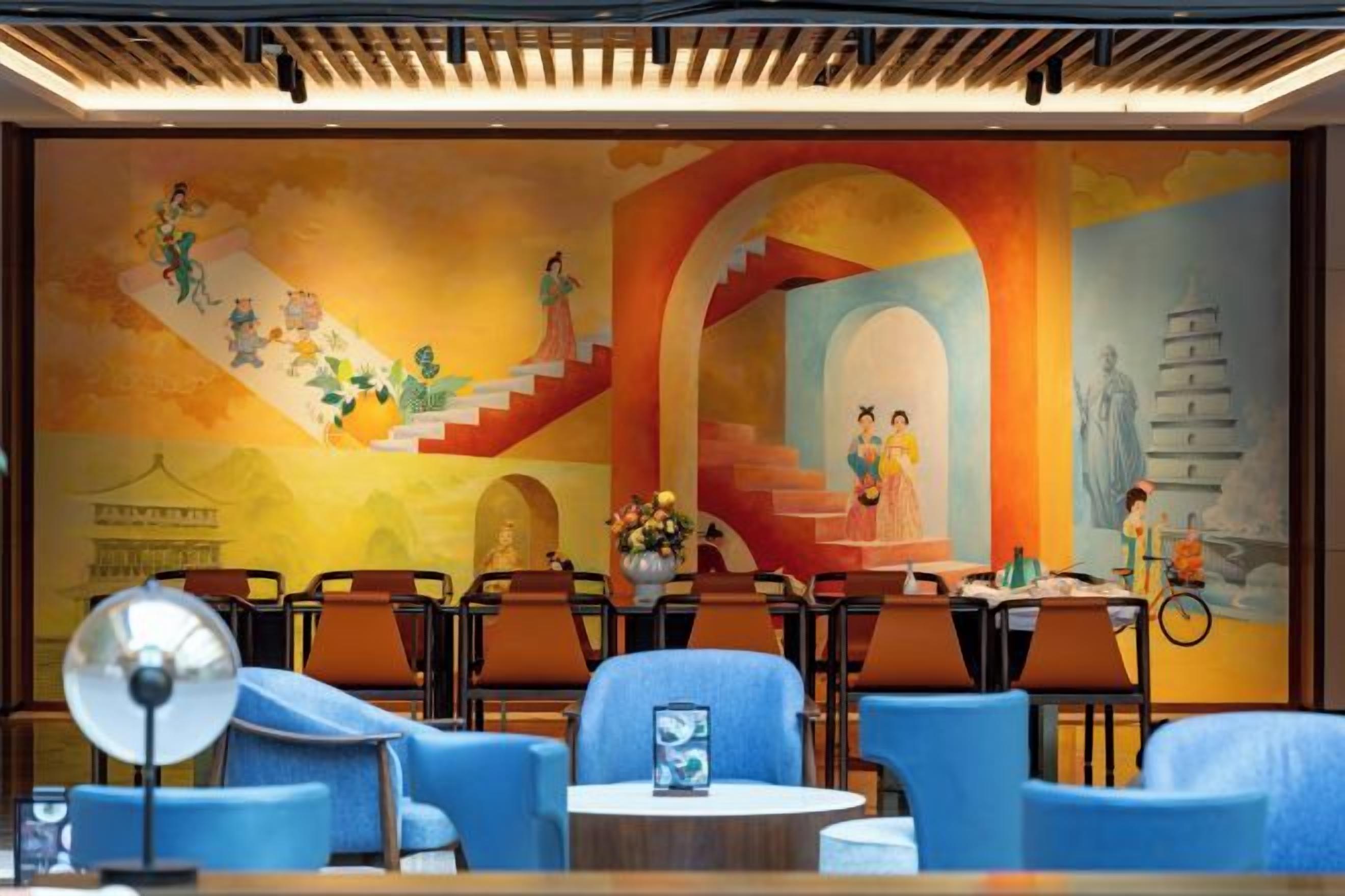 A hotel lobby with a mural, seating area, and a staircase.
