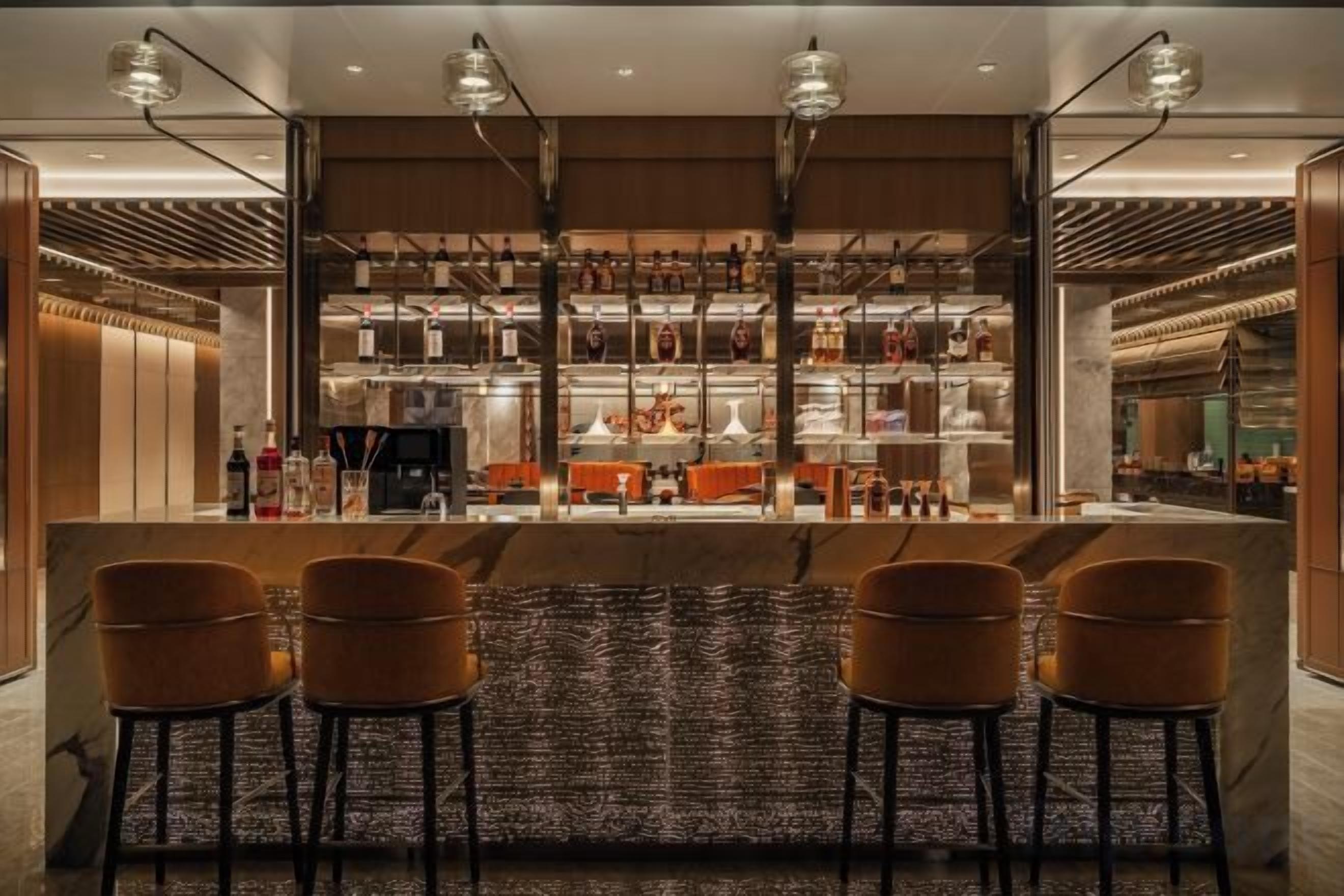 A bar area with a marble countertop, multiple stools, and a well-stocked shelf with bottles.