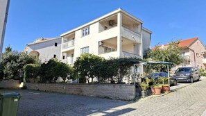 Un immeuble résidentiel à plusieurs étages, doté de balcons, d’une allée pavée et de plantes en pot.