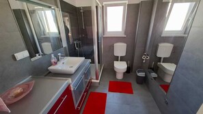 Une salle de bain moderne avec un grand miroir, un lavabo, deux toilettes et un espace douche.