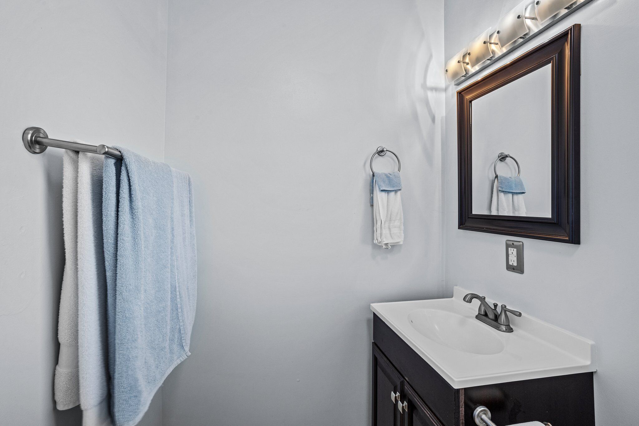 Une salle de bain avec un lavabo blanc, un meuble-lavabo foncé et un miroir avec éclairage intégré.