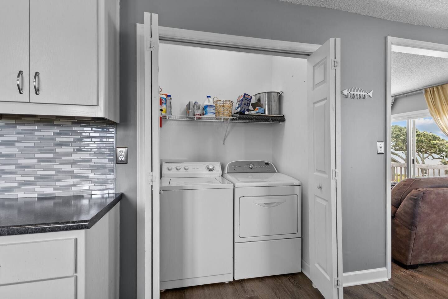 A compact laundry room with a washing machine and dryer, a tiled backsplash, and a shelf with various items.