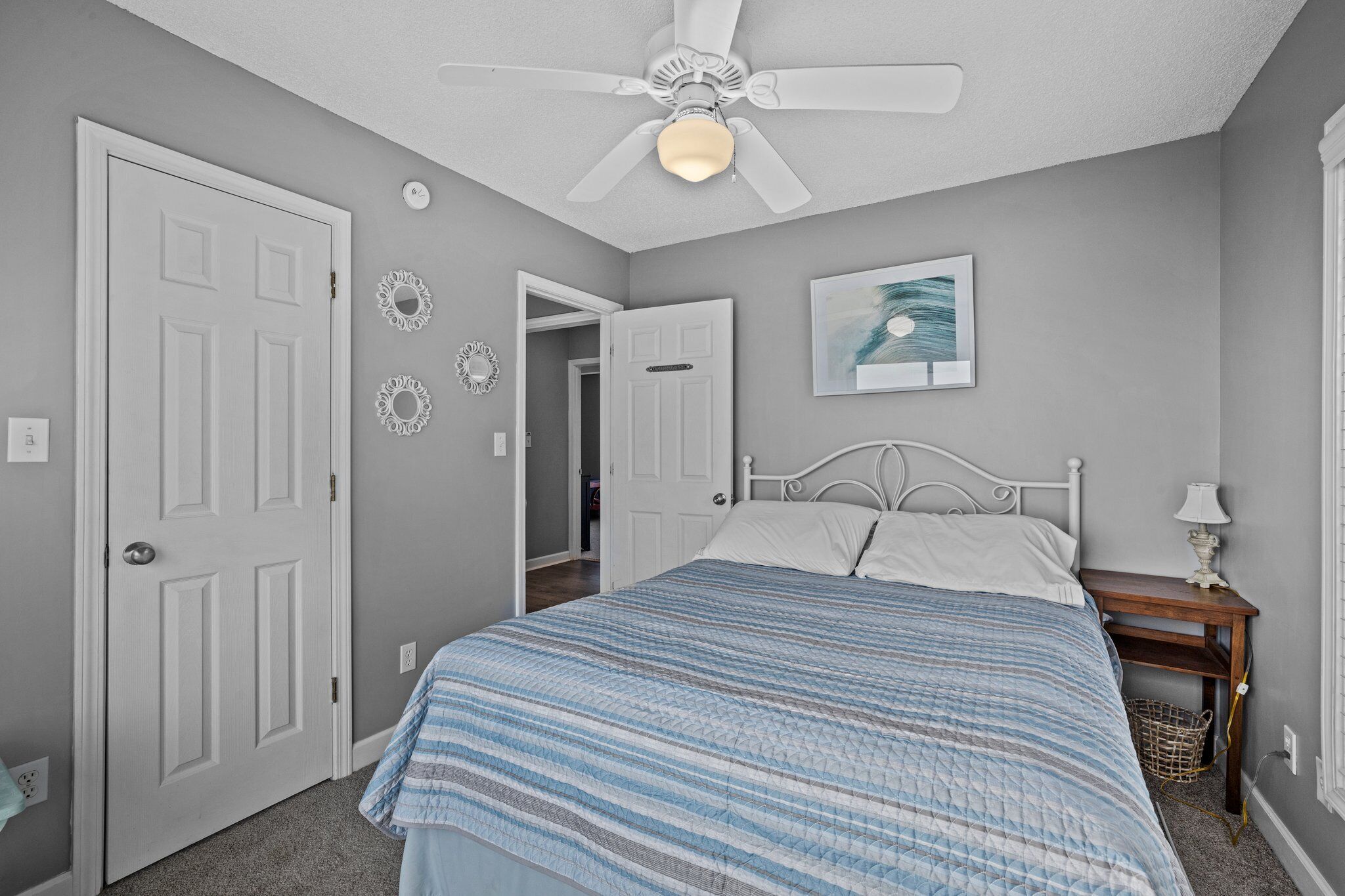 Une chambre à coucher avec un lit, un ventilateur de plafond, une table de chevet avec une lampe et une porte.