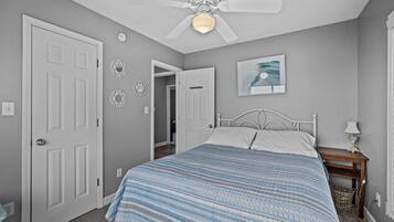 Une chambre à coucher avec un lit, un ventilateur de plafond, une table de chevet avec une lampe et une porte.