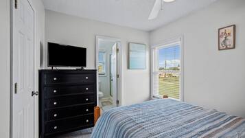 Un dormitorio con cama, cómoda, televisor, ventana con persianas y ventilador de techo.