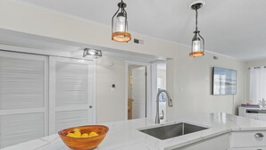 Una cocina moderna con armarios blancos, encimera de mármol, un cuenco de madera con limones e iluminación colgante.