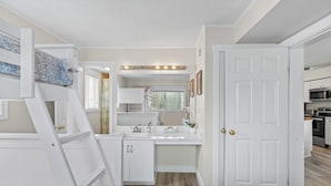 Un dormitorio compacto con literas, un pequeño kitchenette, un baño con tocador y una puerta que da a otra habitación.
