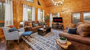A cozy log cabin interior with a wooden interior, a large TV screen displaying 'NETFLIX', and a comfortable seating area with a coffee table. - Large Game Garage, Fire Pit, Hot Tub, Mt. LeConte Views! (Sevierville)