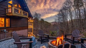 A cabin with a fire pit, outdoor seating, and a deck overlooking a forested area. - Large Game Garage, Fire Pit, Hot Tub, Mt. LeConte Views! (Sevierville)
