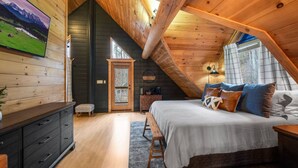 A cozy attic bedroom with a wooden ceiling, a large bed, a dresser, and a TV on the wall. - Large Game Garage, Fire Pit, Hot Tub, Mt. LeConte Views! (Sevierville)