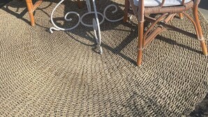 Un espace extérieur aménagé avec des chaises en osier et une table en verre, agrémenté d’une petite nappe blanche et d’un vase rempli de fleurs.
