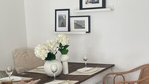 Un coin repas avec une table en bois foncé, des chaises blanches et un vase rempli de fleurs blanches. Des tableaux encadrés sont accrochés au mur, au-dessus de la table.