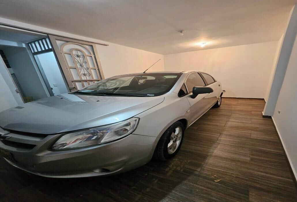 A car parked inside a room with wooden flooring and white walls.