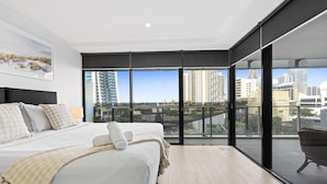 A modern bedroom with a large bed, a view of the city, and a balcony. - Comfortable 1 Bedroom + Study Apartment - Q Stay (Surfers Paradise)