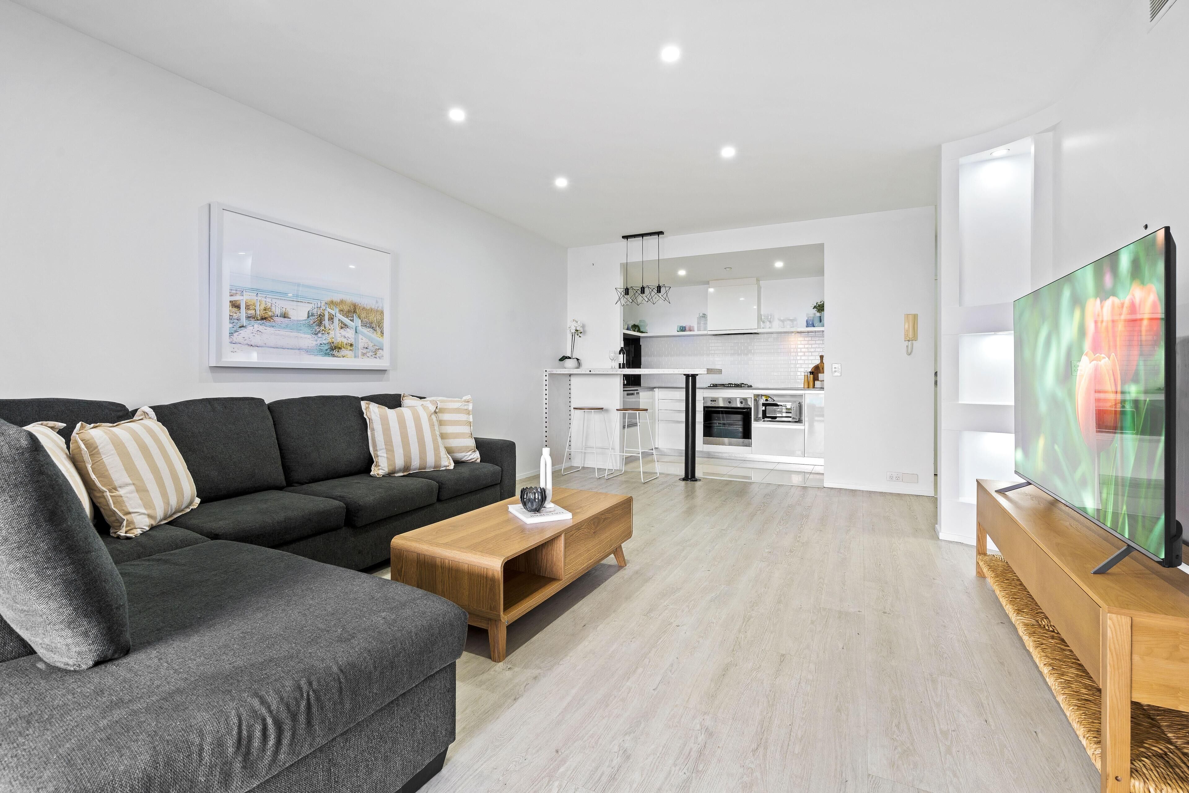 Una sala de estar moderna con un sofá gris, una mesa de centro de madera y un televisor de pantalla plana.