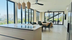 Una cocina moderna con una isla grande, ventanas amplias y un comedor con una escalera que da al exterior.