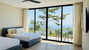 Un dormitorio con dos camas, un ventilador de techo y un gran ventanal corredizo que da a una zona de estar exterior con vistas al paisaje.